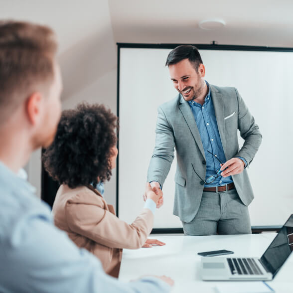 Three people in a meeting room. Two of them are shaking hands.