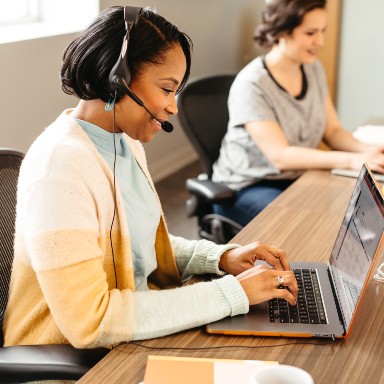 A seated customer service at work wearing a headphone.