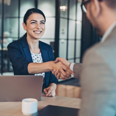 Two seated business people shaking hands from across a table.