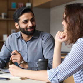 Deux collaborateurs discutent assis à une table de travail.