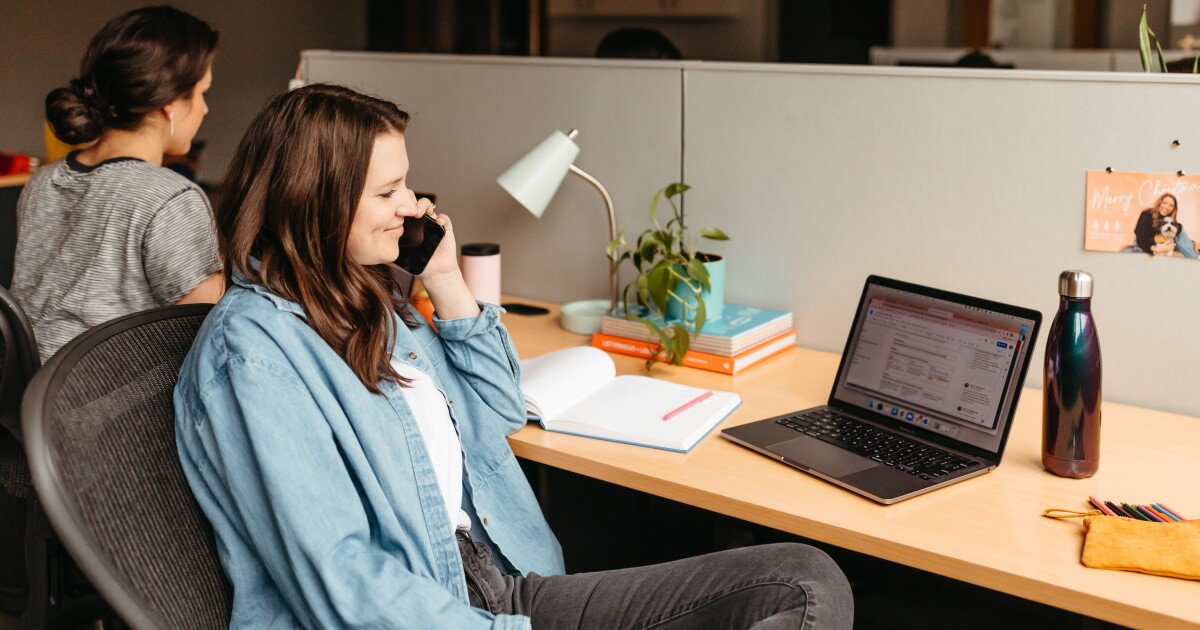 Woman talking on phone while looking at laptop.