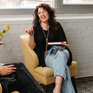 A woman sits on on a chair while holding a book