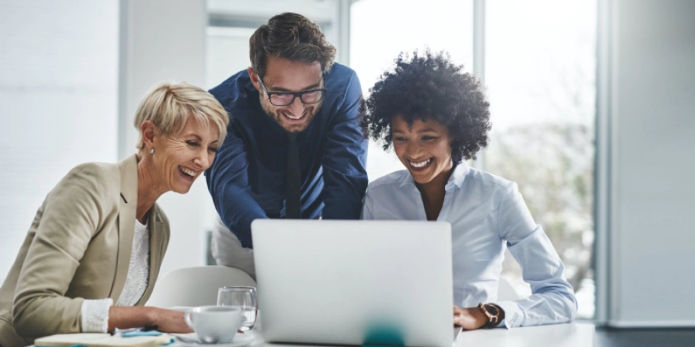 Three smiling office workers looking at a laptop screen.