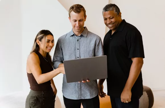 Three people smile while looking at a laptop