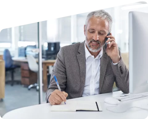 A man talking on his mobile and making notes on a paper pad.