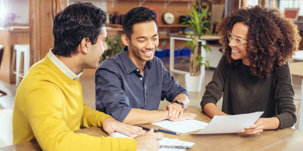 Three individuals reviewing documents at a table.