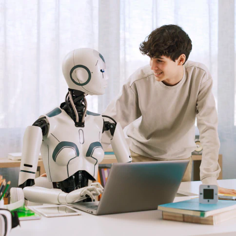 A person interacting with person like robot that is seated in front of a laptop.