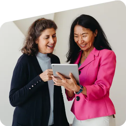 Two smiling women looking at notebook.