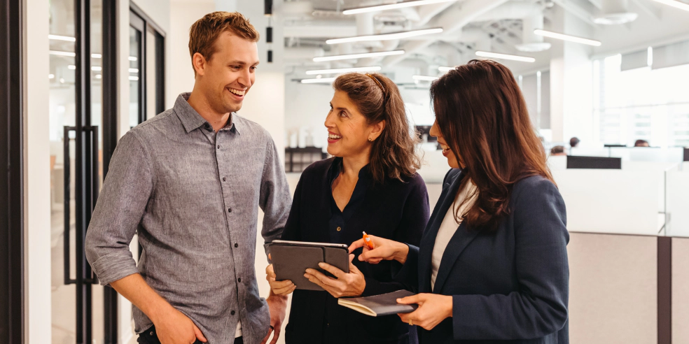 Three people standing in an office looking at a tablet screen.