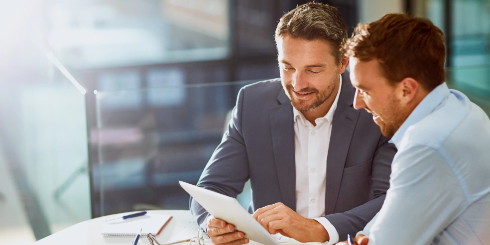 A financial advisor is seated next to a client while pointing to a laptop.